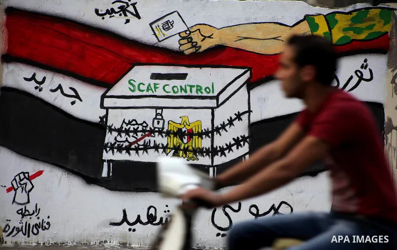 Egyptians walk past graffiti depicting a chained ballot box being controlled by the ruling military council at Tahrir Square in Cairo on May 25, 2012. Egyptians reacted nervously to the first results of their presidentia...