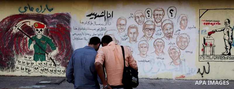 Egyptians walk in front of a wall sprayed graffiti at Tahrir Square in Cairo May 30, 2012. An arson attack on the headquarters of one of the two candidates in Egypt's presidential election has marred campaigning for the...