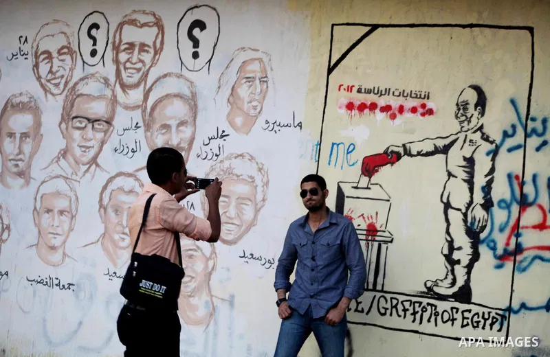 Egyptians walk in front of a wall sprayed graffiti at Tahrir Square in Cairo May 30, 2012. An arson attack on the headquarters of one of the two candidates in Egypt's presidential election has marred campaigning for the...