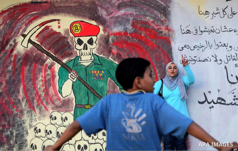 Egyptians walk in front of a wall sprayed graffiti at Tahrir Square in Cairo May 30, 2012. An arson attack on the headquarters of one of the two candidates in Egypt's presidential election has marred campaigning for the...