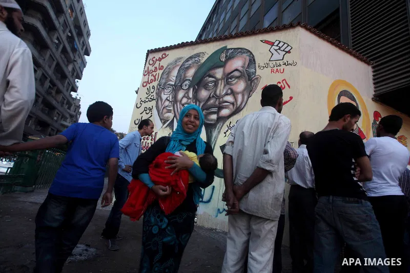 Egyptians walk in front of a wall sprayed graffiti at Tahrir Square in Cairo May 30, 2012. An arson attack on the headquarters of one of the two candidates in Egypt's presidential election has marred campaigning for the...