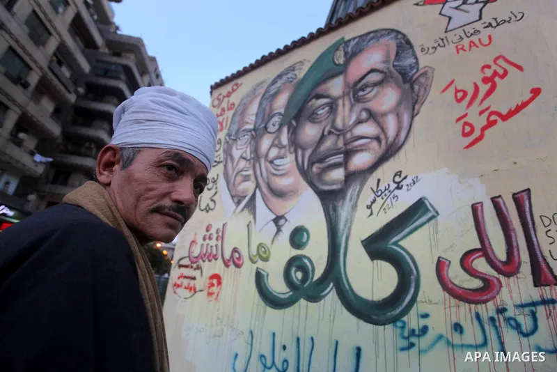 Egyptians walk in front of a wall sprayed graffiti at Tahrir Square in Cairo May 30, 2012. An arson attack on the headquarters of one of the two candidates in Egypt's presidential election has marred campaigning for the...