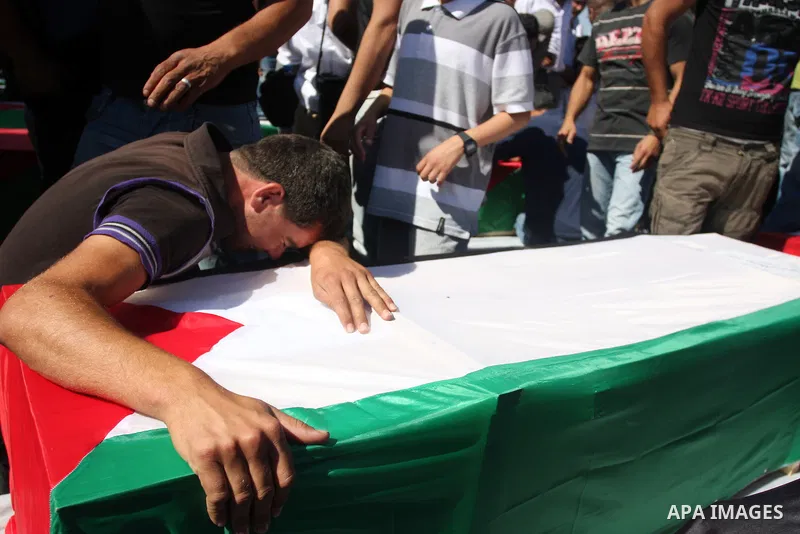 Palestinian man mourn over a flag-draped coffin prior to the funeral of 91 Palestinians whose remains were returned by Israel at the Palestinian leadership headquarters in the West Bank city of Ramallah on May 31, 2012....