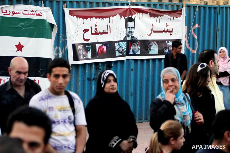Protesters stand in front of a banner of Syria's President Bashar al-Assad during a protest against the weekend massacre of Houla, in front of the Syrian embassy in Cairo, Egypt, 31 May 2012. A massacre was reported in t...