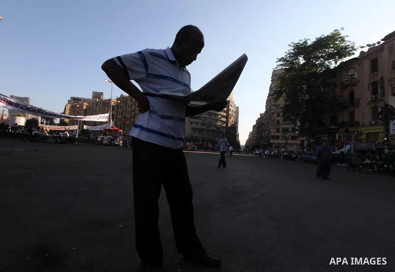 An Egyptian protester reads newspaper on the street under mural in Cairo's landmark Tahrir Square on June 6, 2012, as people demonstrated to protest against verdicts handed down in ex-president Hosni Mubarak's murder tri...