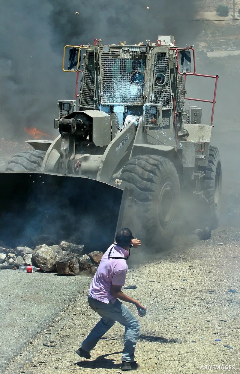 Palestinian protester throws stones toward Israeli military bulldozer during clashes after a demonstration against the nearby Jewish settlement of Kdumim, in the West Bank village of Kfar Kadum, near Nablus June 8, 2012....
