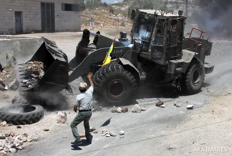Palestinian protester throws stones toward Israeli military bulldozer during clashes after a demonstration against the nearby Jewish settlement of Kdumim, in the West Bank village of Kfar Kadum, near Nablus June 8, 2012....