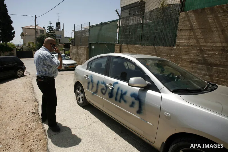 A Palestinian man gestures towards a car sprayed with graffiti written in Hebrew that reads, "Ulpena" referring to the Jewish outpost built illegally in the West Bank and which is earmarked to be relocated following a su...