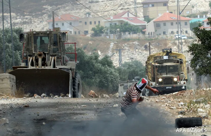 A Palestinian protester throws stone at an Israeli army bulldozer during clashes in the northern West Bank village of Kufr Qaddum, after the weekly protest against the expansion of the nearby Jewish settlement of Kdumim,...