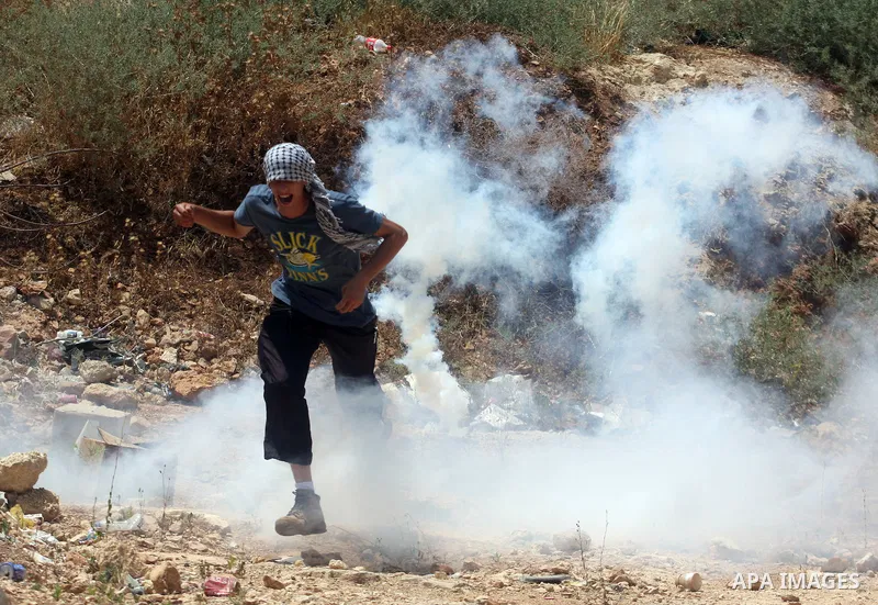 A Palestinian protester takes cover from tear gas fired by Israeli soldiers during clashes in the West Bank village of Nabi Saleh, near Ramallah, on June 15, 2012, following a demonstration against the confiscation of Pa...