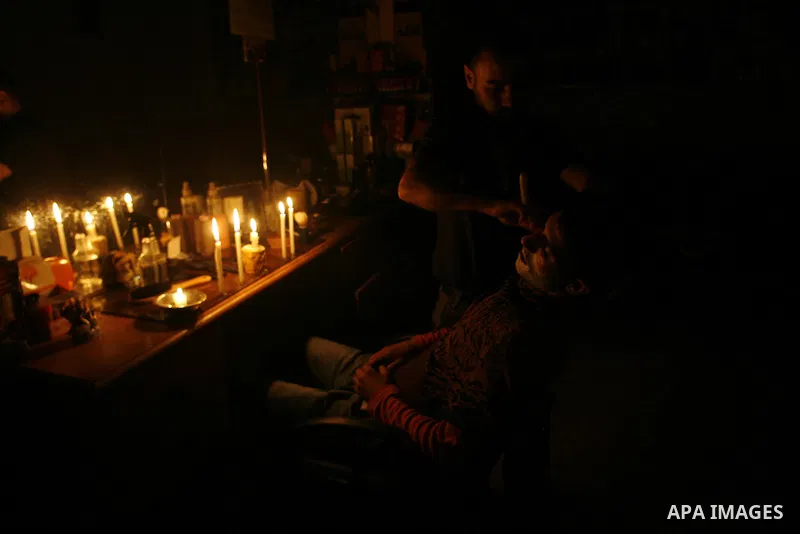A Palestinian barber cuts hair for youths and lighting a candle during a power outage in a barber shop in Rafah, southern Gaza Strip on June 16, 2012. Photo by Eyad Al Baba