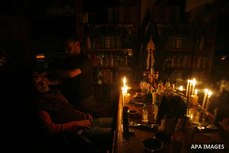 A Palestinian barber cuts hair for youths and lighting a candle during a power outage in a barber shop in Rafah, southern Gaza Strip on June 16, 2012. Photo by Eyad Al Baba