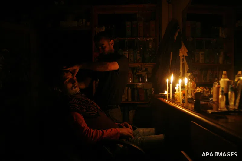 A Palestinian barber cuts hair for youths and lighting a candle during a power outage in a barber shop in Rafah, southern Gaza Strip on June 16, 2012. Photo by Eyad Al Baba