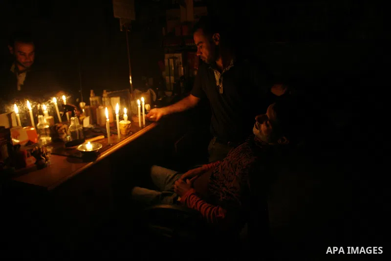 A Palestinian barber cuts hair for youths and lighting a candle during a power outage in a barber shop in Rafah, southern Gaza Strip on June 16, 2012. Photo by Eyad Al Baba