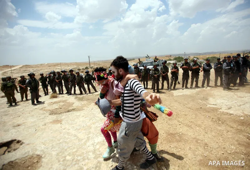 Foreign activists and Palestinians dressed as clowns gesture in front of Israeli policemen during a protest in the southern West Bank village of Susia near Hebron city on June 22, 2012 where Israel has recently served or...