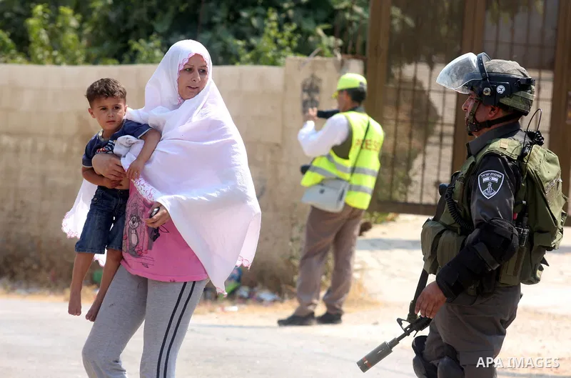 A Palestinian woman carries her child during clashes with Palestinian protesters in the West Bank village of Nabi Saleh, near Ramallah, on June 22, 2012, following a demonstration against the confiscation of Palestinian...