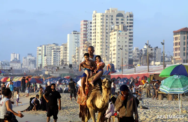 Palestinians ride a camel as others enjoy swimming in the sea on Gaza's beach on 27 June 2012 in Gaza. Photo by Majdi Fathi
