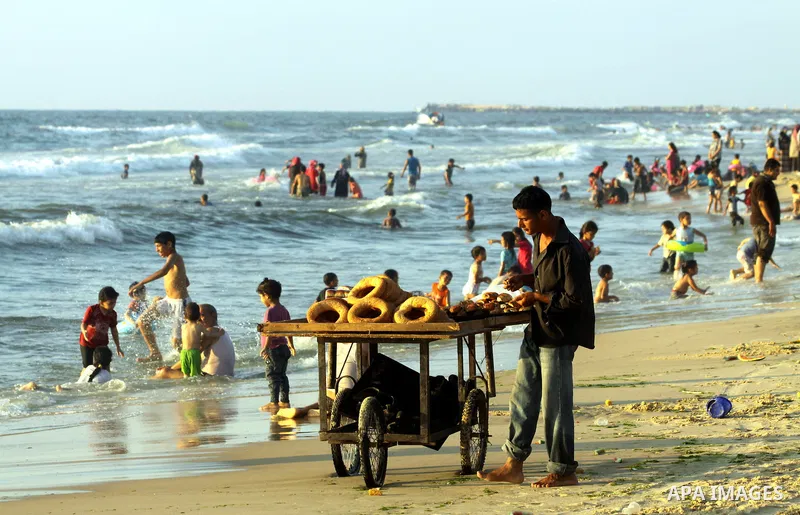 A Palestinian man sells bread as others enjoy swimming in the sea on Gaza's beach on 27 June 2012 in Gaza . Photo by Majdi Fathi