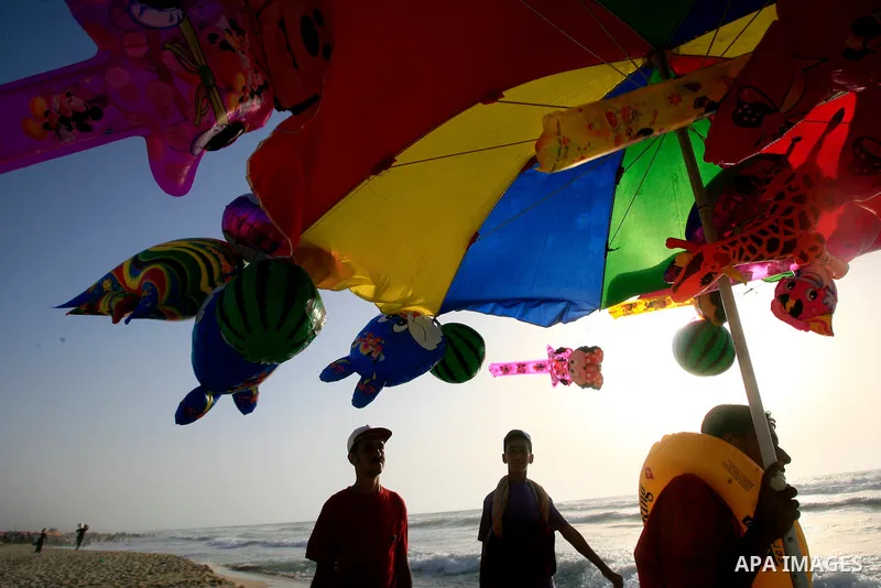 A Palestinian man sells toys as others enjoy swimming in the sea on Rafah's beach in the southern of Gaza strip,on 29 June 2012. Photo by Eyad Al Baba