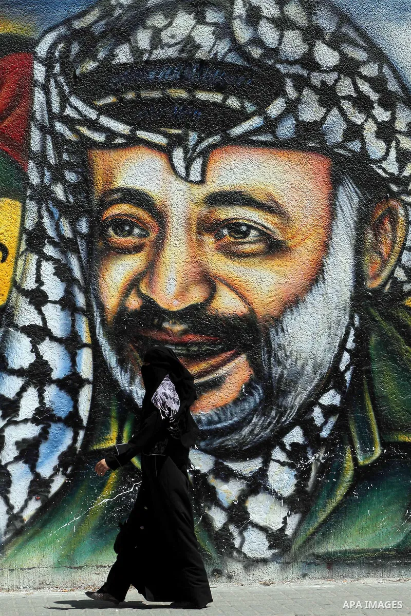 A Palestinian woman walks past a mural depicting late Hamas spiritual leader Sheikh Ahmed Yassin (L) and late Palestinian leader Yasser Arafat (R) in Gaza City on July 4, 2012. Arafat, who died in 2004, was poisoned by p...