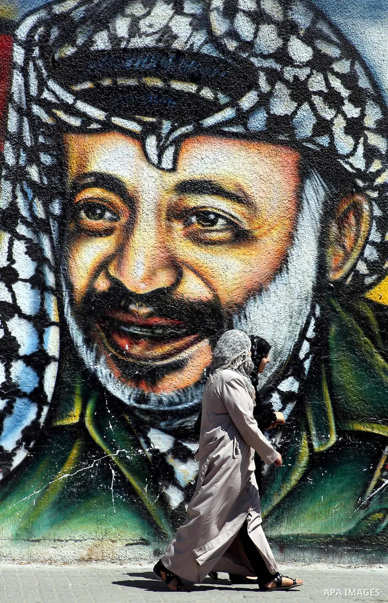 Palestinian women walk past a mural depicting late Hamas spiritual leader Sheikh Ahmed Yassin (L) and late Palestinian leader Yasser Arafat (R) in Gaza City on July 4, 2012. Arafat, who died in 2004, was poisoned by polo...