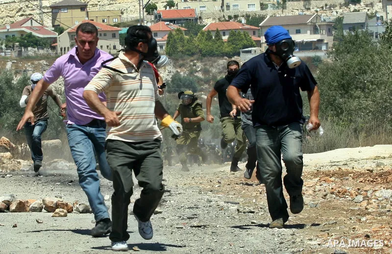 Palestinians run away cover from teargas during clashes with Israeli border policemen following a protest against the expansion of the nearby Jewish settlement of Kdumim, in the northern West Bank village of Kufr Qaddum,...