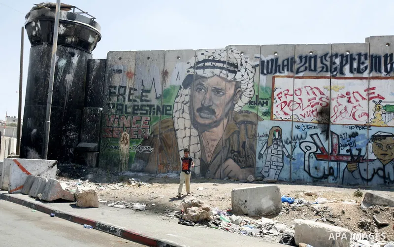 A Palestinian boy walks past a mural of late Palestinian leader Yasser Arafat on a section of Israel's controversial separation barrier at Qalandia checkpoint, between Jerusalem and Ramallah on July 6, 2012. The Palestin...