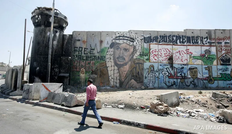 A Palestinian man walks past a mural of late Palestinian leader Yasser Arafat on a section of Israel's controversial separation barrier at Qalandia checkpoint, between Jerusalem and Ramallah on July 6, 2012. The Palestin...