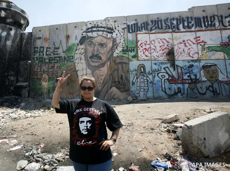 An Egyptian woman wearing a T-shirt with portrait of Argentinian-Cuban guerrilla Che Guevara poses for a picture in front of a mural of late Palestinian leader Yasser Arafat on a section of Israel's controversial separat...