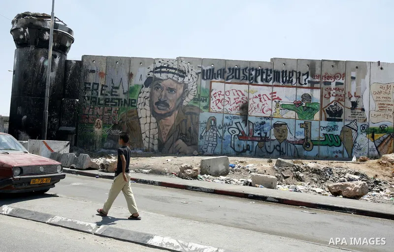 A Palestinian boy walks past a mural of late Palestinian leader Yasser Arafat on a section of Israel's controversial separation barrier at Qalandia checkpoint, between Jerusalem and Ramallah on July 6, 2012. The Palestin...