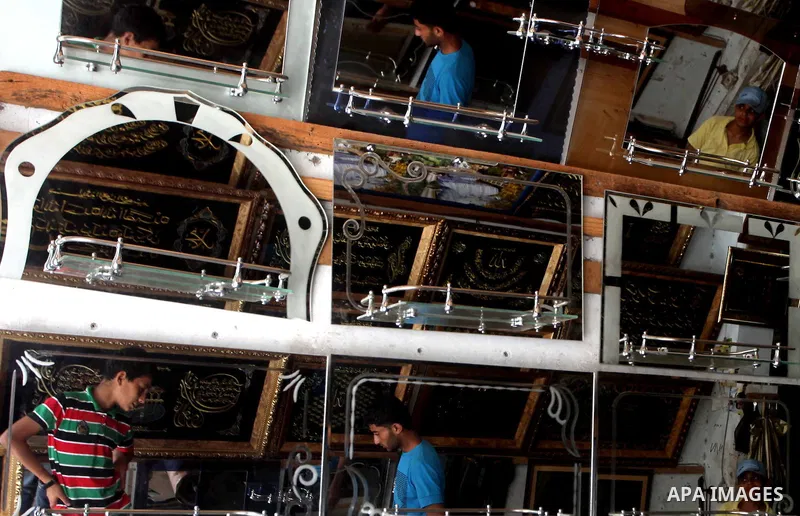 Palestinian workers reflected in mirrors for sale as he walks through a traditional market in the refugee camp of Jabaliya, in the northern Gaza Strip, 07 July 2012 . Photo by Ashraf Amra