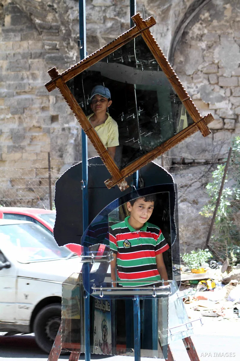 Palestinians are reflected in mirrors for sale as they walk through a traditional market in the refugee camp of Jabaliya, in the northern Gaza Strip, 07 July 2012 . Photo by Ashraf Amra