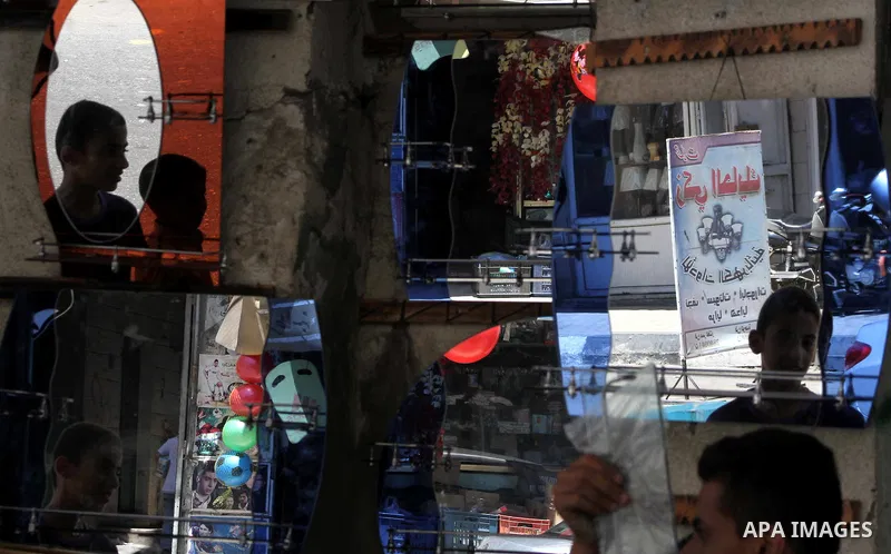 Palestinian workers reflected in mirrors for sale as he walks through a traditional market in the refugee camp of Jabaliya, in the northern Gaza Strip, 07 July 2012 . Photo by Ashraf Amra