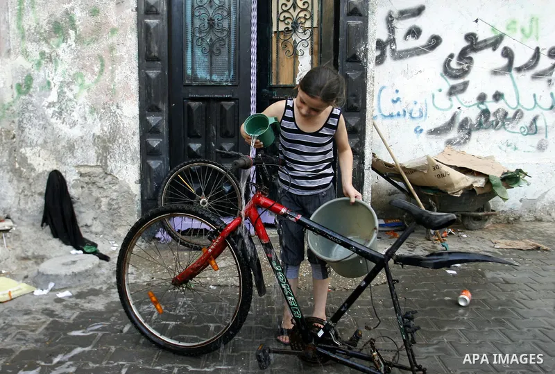 A Palestinian child cleans the motorcycle at water as hot weather hits the southern Gaza Strip. Photo by Eyad Al Baba