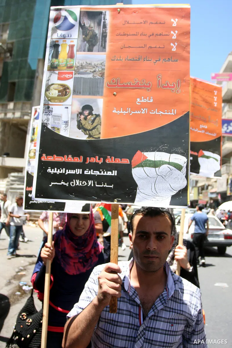 Palestinian protestors hold posters and graphics during a protest demanding Palestinian merchants to boycott Israeli settlement products and goods, and support national economy in the West Bank city of Ramallah ,on July...