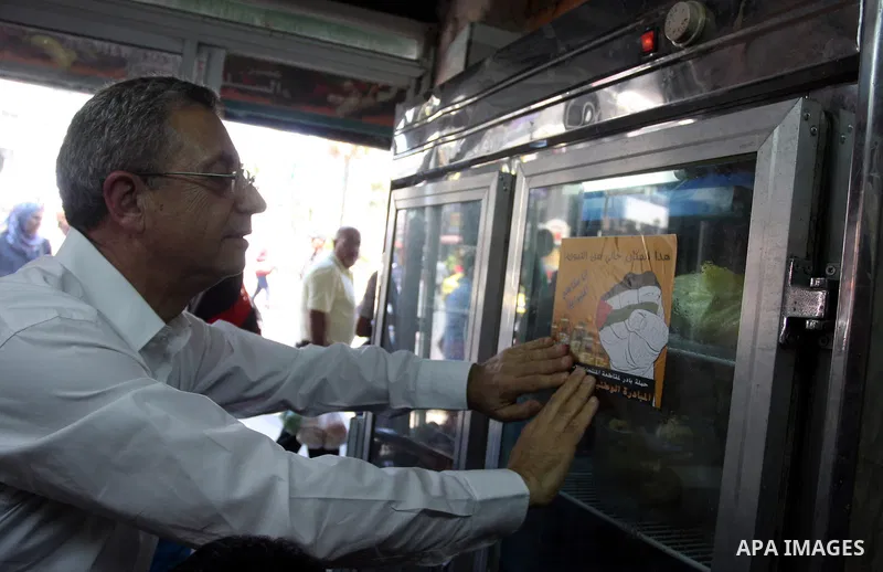 Mustafa al-Barghouthi, Secretary General of the Palestinian National Initiative hangs a placard during a protest demanding Palestinian merchants to boycott Israeli settlement products and goods, and support national econ...