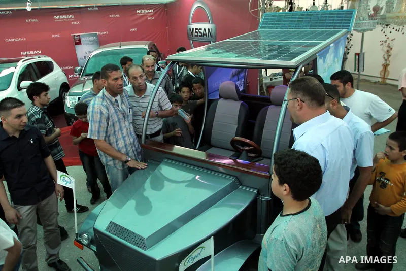 Palestinians inspect the first Palestinian electric car during an international environment expo held in the West Bank city of Hebron, on 17 July 2012. The exhibitors attended the expo bringing such new technologies and...