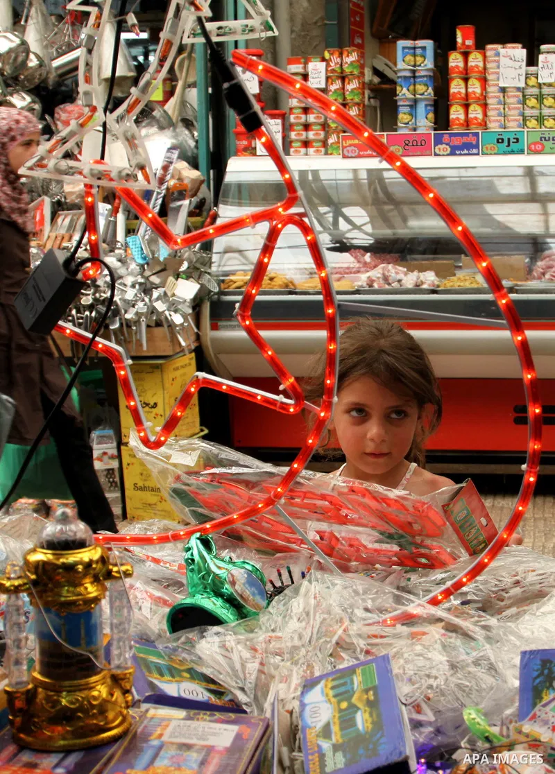 A Palestinian girl looks at a vendor as he decorates his shop with an electric crescent in preparation for the holy month of Ramadan in the West Bank city of Nablus, on July 18, 2012 . Islam's holy month of Ramadan will...