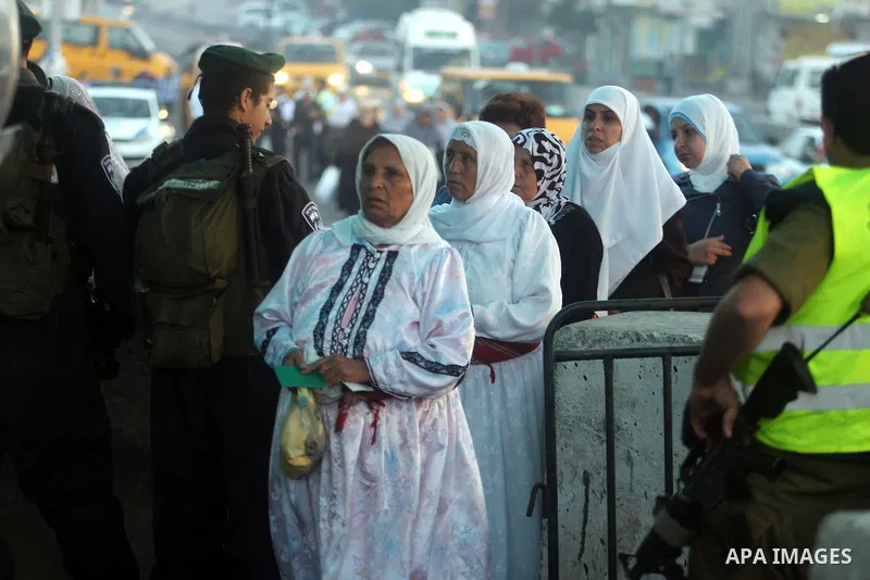 An Israeli border police officer checks documents of Palestinian women who wait to cross the Qalandia checkpoint on the outskirts of the West Bank city of Ramallah on July 20, 2012 as they head to the Al-Aqsa mosque comp...