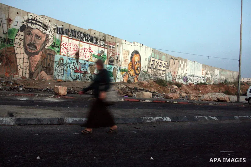 Palestinian muslim worshippers walk past a graffiti painted section of the separation wall at the Qalandia checkpoint on the outskirts of the West Bank city of Ramallah on July 20, 2012 as they head to the Al-Aqsa mosque...