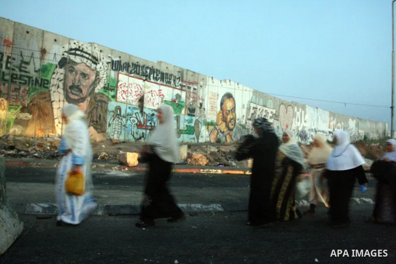 Palestinian muslim worshippers walk past a graffiti painted section of the separation wall at the Qalandia checkpoint on the outskirts of the West Bank city of Ramallah on July 20, 2012 as they head to the Al-Aqsa mosque...