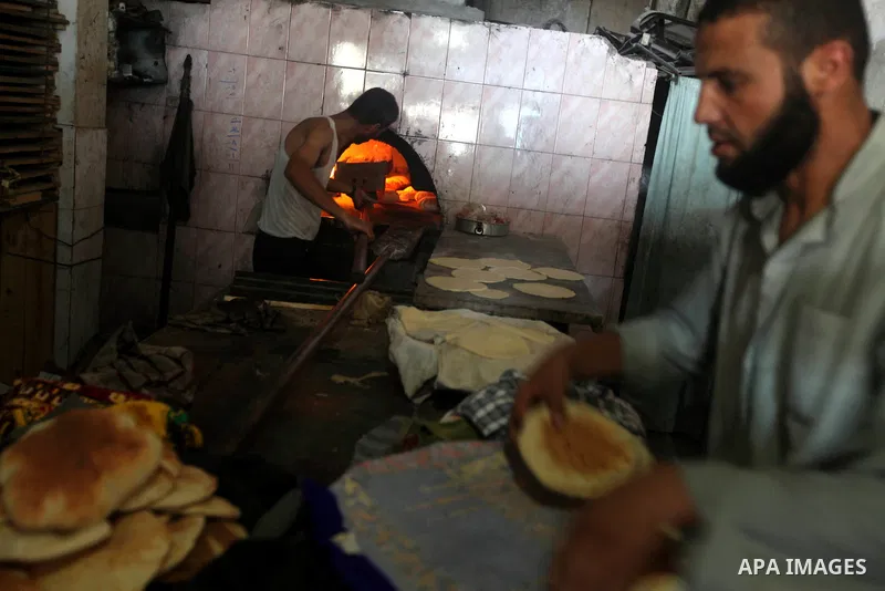 A Palestinian man helps baker to bake bread in his traditional mud oven during Ramadan in Jabalya refugee camp, northen Gaza Strip on July 23, 2012. Muslims around the world abstain from eating, drinking and conducting s...