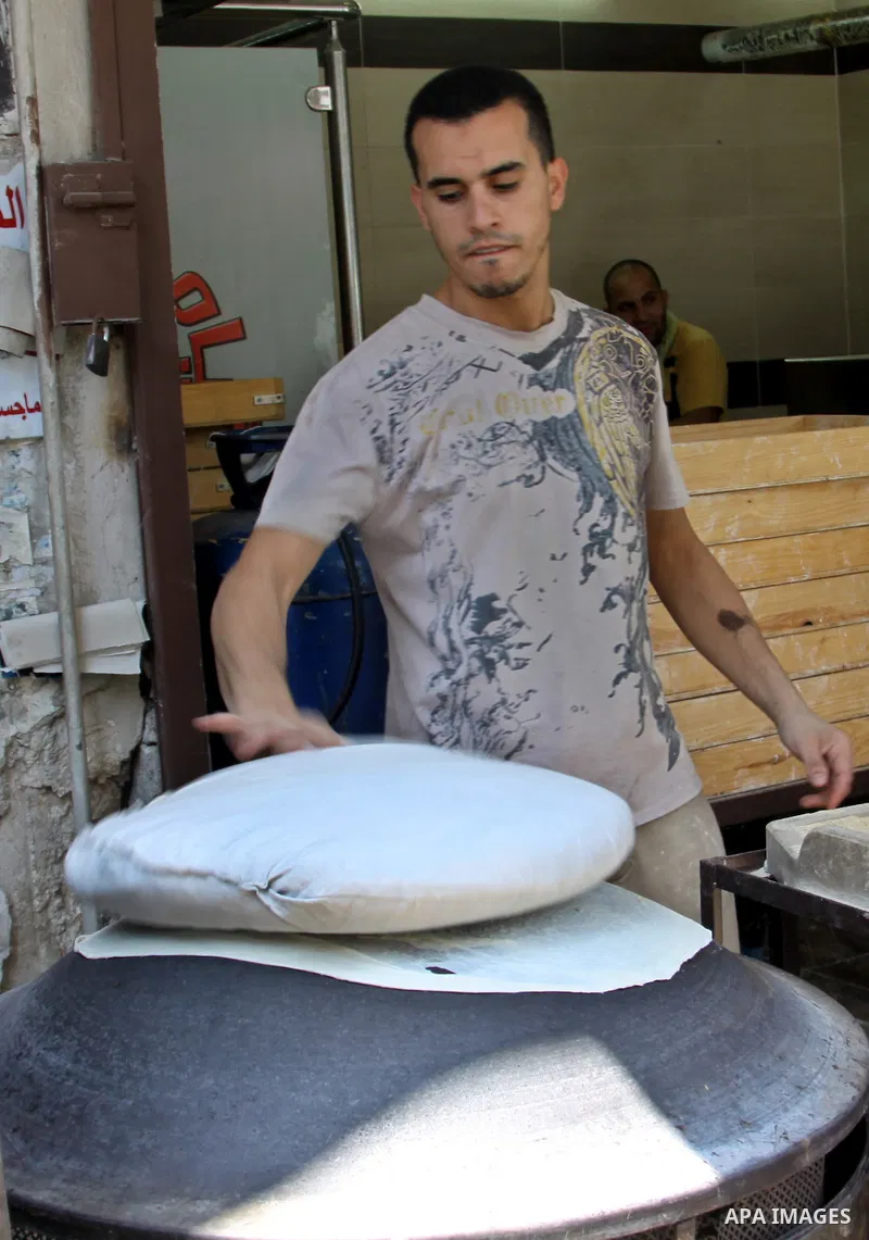 A Palestinian man bakes loaves of bread in his traditional mud oven during Ramadan in the West Bank city of Nablus on July 25, 2012. Muslims around the world abstain from eating, drinking and conducting sexual relations...