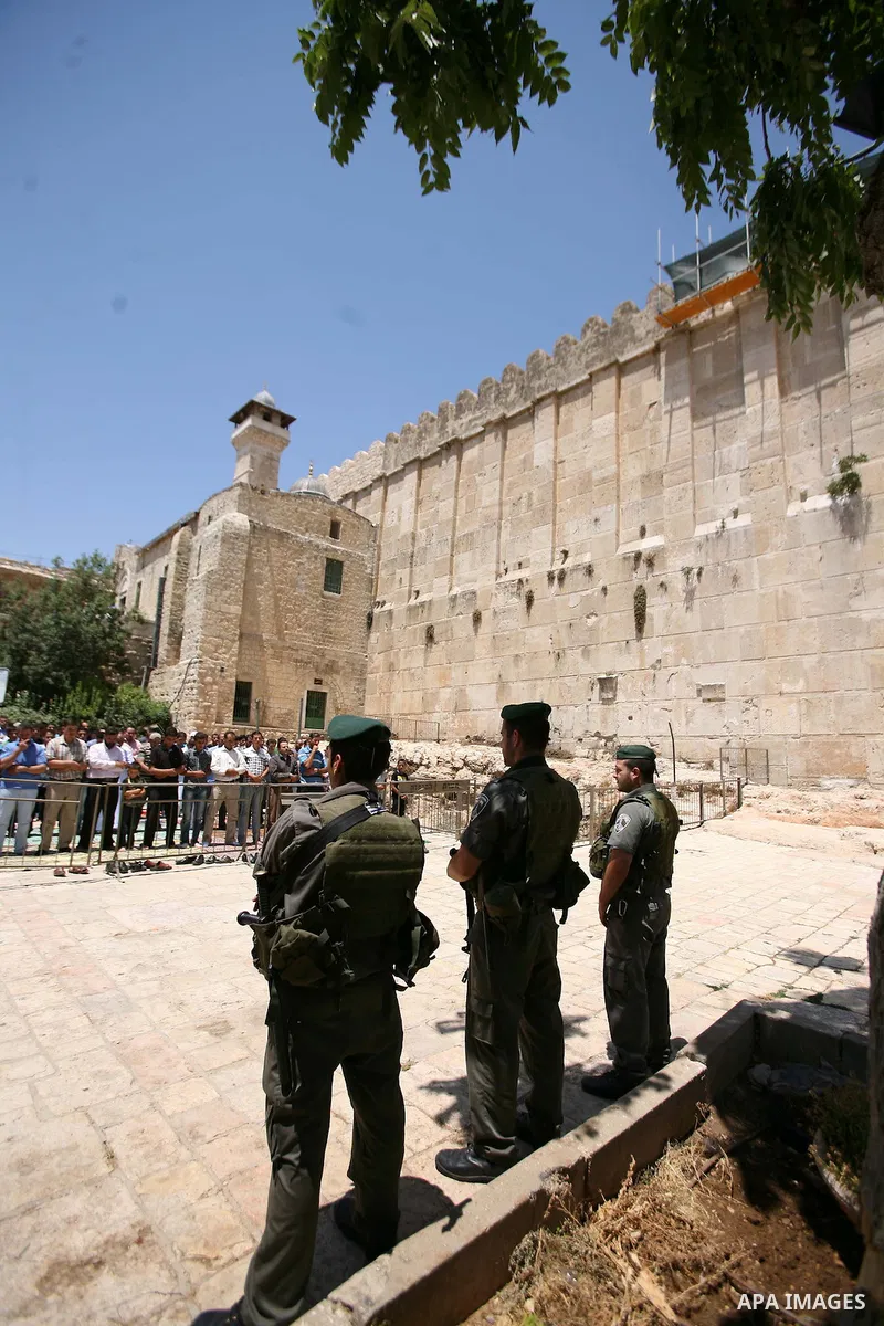Israeli border policemen stand guard as Palestinian men perform the second Friday prayers of the Muslim fasting month of Ramadan outside the Ibrahimi Mosque or the Tomb of the Patriarchs in the West Bank city of Hebron o...