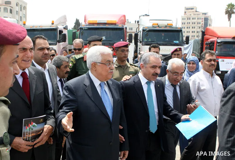 Palestinian President Mahmoud Abbas, os accompanied by other officials as he waves to a convoy of trucks carrying food and medical supplies, which reportedly were provided by the Palestinian people, leaving Ramallah boun...