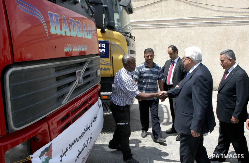 Palestinian President Mahmoud Abbas, os accompanied by other officials as he waves to a convoy of trucks carrying food and medical supplies, which reportedly were provided by the Palestinian people, leaving Ramallah boun...