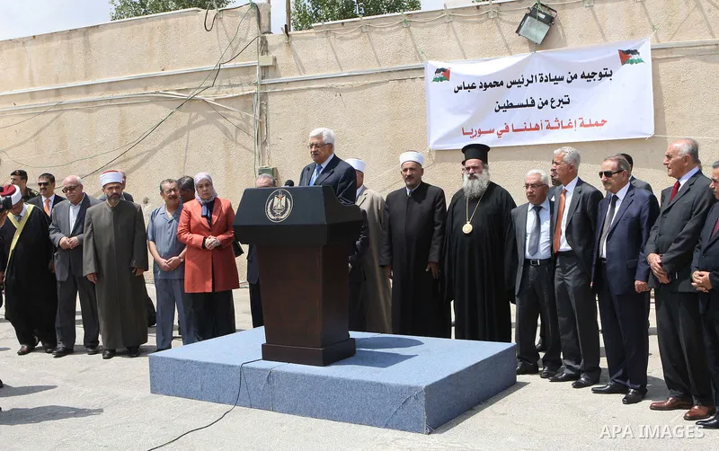 Palestinian President Mahmoud Abbas, os accompanied by other officials as he waves to a convoy of trucks carrying food and medical supplies, which reportedly were provided by the Palestinian people, leaving Ramallah boun...