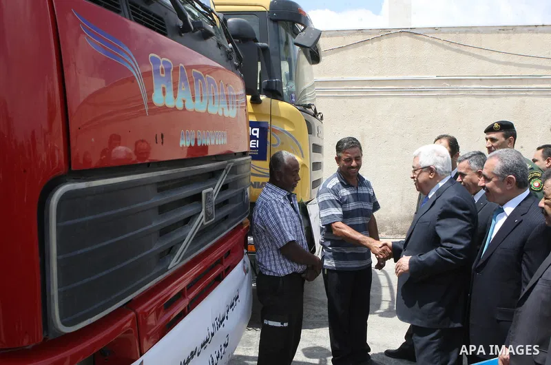 Palestinian President Mahmoud Abbas, os accompanied by other officials as he waves to a convoy of trucks carrying food and medical supplies, which reportedly were provided by the Palestinian people, leaving Ramallah boun...
