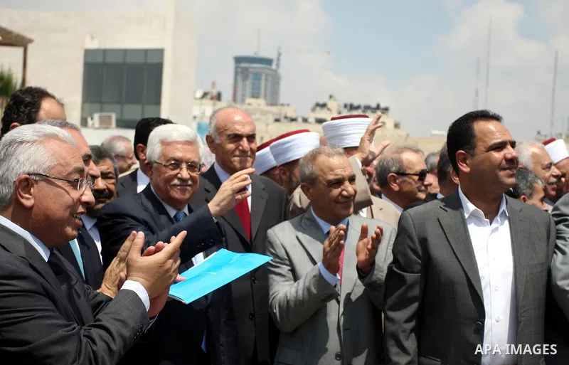 Palestinian President Mahmoud Abbas, accompanied by other officials as he waves to a convoy of trucks carrying food and medical supplies, which reportedly were provided by the Palestinian people, leaving Ramallah bound f...