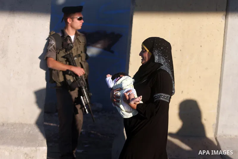 A Palestinian woman walks past an Israeli border police officer during cross the military checkpoint of Qalandia, North of Jerusalem, in the West Bank, 10 August 2012, on their way to Jerusalem to attend the Ramadan Frid...